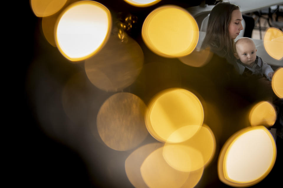 Vlada Yushchenko, a 19-year-old Ukrainian refugee, holds her son Daniel, seen through the lights of a Christmas tree, during an interview with The Associated Press in Brasov, Romania, Thursday, Feb. 2, 2023. Yushchenko was still in her teens and nearly three months pregnant when she hugged her husband at the border, turned away and walked into Moldova. Now she’s in Romania, one of the millions of Ukrainians forced to flee Russia’s invasion of their country. Her baby, Daniel, was born there eight months ago and still hasn’t met his father Yaroslav, who is 21 and, like most men of fighting age, prohibited from leaving Ukraine. (AP Photo/Vadim Ghirda)