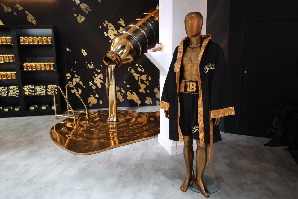 Inside of the Prime store in London, with a huge gold bottle pouring a gold liquid and a gold mannequin wearing boxing clothing.