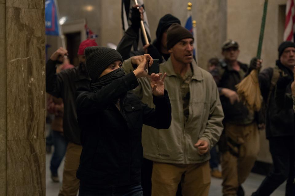 Bradley Jackson wearing all black and a face mask, holding up an iPhone at a re-creation of the Jan. 6 insurrection.