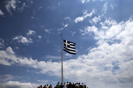 People stand under a Greek national flag atop the Acropolis hill in Athens June 5, 2015. REUTERS/Alkis Konstantinidis