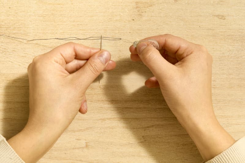 Overhead shot of two hands using a needle threader to thread a needle.