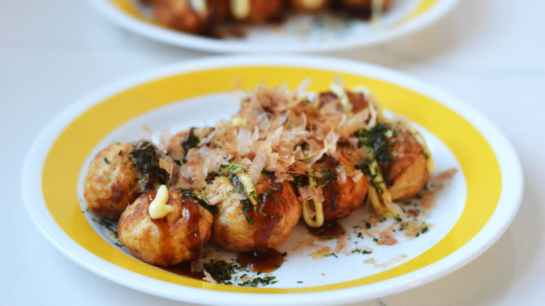 Close-up of 8 takoyaki balls on a yellow-rimmed plate