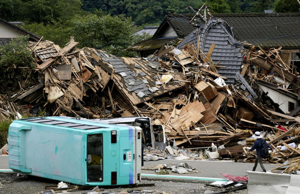 People walks past an overturned cars and the houses damaged by a flooded river in Kuma village, Kumamoto prefecture, southern Japan Wednesday, July 8, 2020. Floodwaters flowed down streets in southern Japanese towns hit by heavy rains. (Koji Harada/Kyodo News via AP)