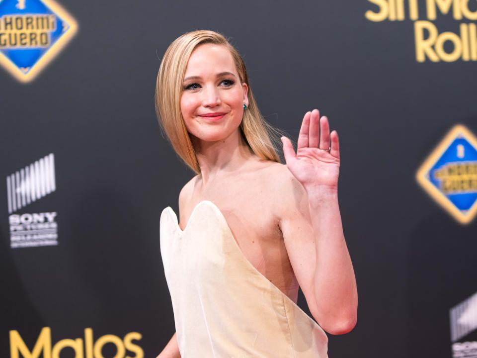 Jennifer Lawrence waving to photographers while wearing her beige midi dress and walking to the left.