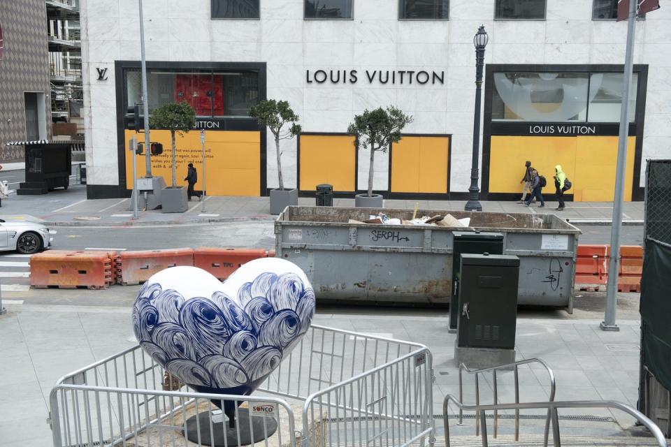 A small number of people walk past a boarded up retail shop