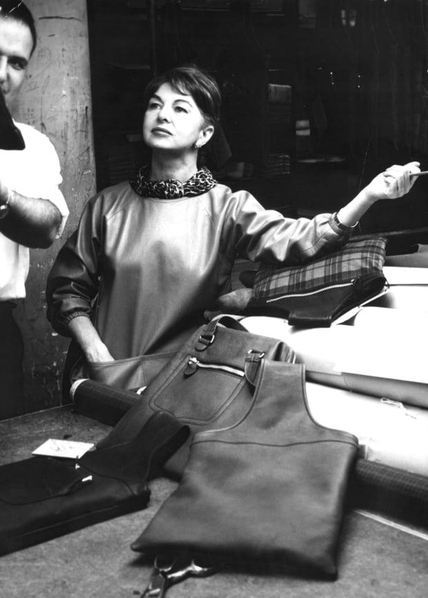 Bonnie Cashin pictured behind-the-scenes surrounded by several of her classic designs, including a crossbody and tote bag.