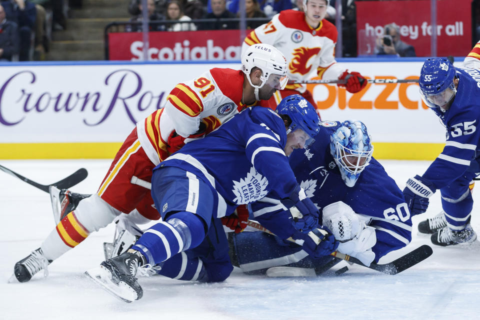 Calgary Flames centre Nazem Kadri (91) falls onto Toronto Maple Leafs defenceman Jake McCabe (22) as goaltender Joseph Woll (60) tries to keep the puck out of the net during the first period of an NHL hockey game Friday, Nov. 10, 2023, in Toronto. (Cole Burston/The Canadian Press via AP)