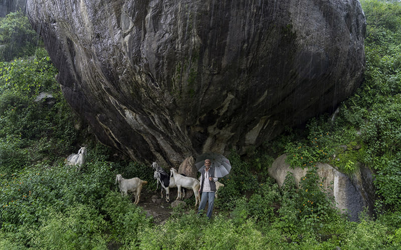 A shepherd with his flock shelters from the rain under a huge boulder