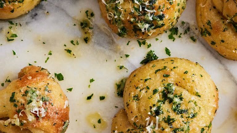 close up of garlic knots topped with parsley and parmesan on a marble background