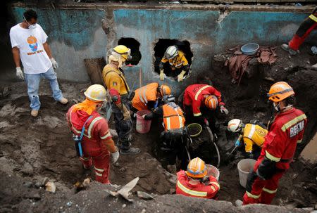 Alejandro Esqueque (L) observes as rescue workers unearth the wheelchair of his mother, after the eruption of the Fuego volcano, in San Miguel Los Lotes in Escuintla, Guatemala June 15, 2018. REUTERS/Luis Echeverria/Files