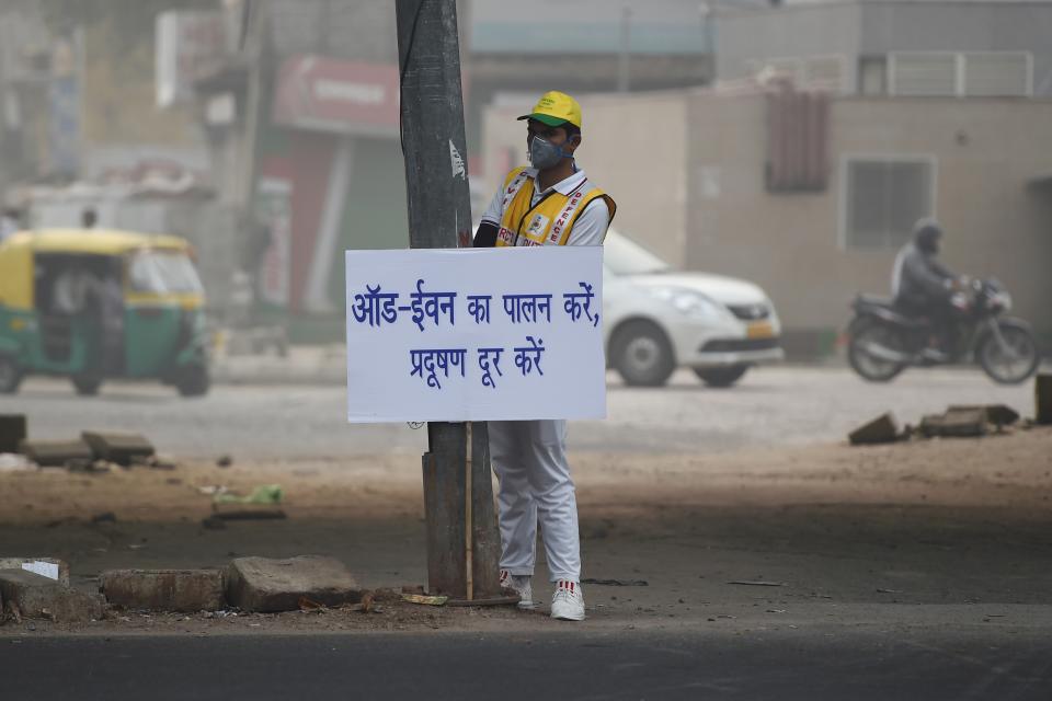 A volunteer from civil defence displays a placard to aware drivers on a street after the local government ordered half of the city's private cars to be taken off the road based on an odd-even registration plate system to help reduce air pollution, in New Delhi on Nov. 4, 2019. (Photo: Money Sharma/AFP via Getty Images)