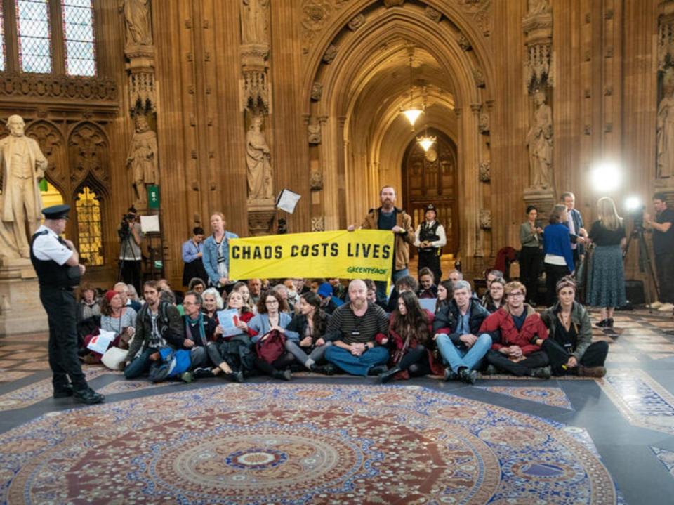 Climate and energy crisis activists unfurl a banner reading ‘Chaos costs lives’ in the Central Lobby in parliament (Suzanne Plunkett/Greenpeace)