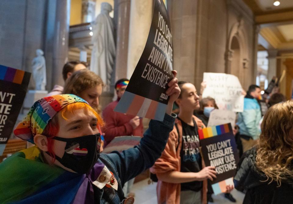 Jay Fassl holds up sign as people protest against SB 480, a total ban on affirming care for transgender youth, while the Indiana House public health committee has a hearing Tuesday, March 21, 2023 in the House Chamber of the Indiana State Capitol building.