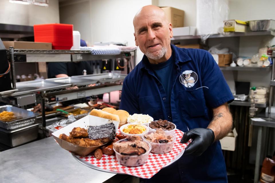 Road Hawg Barbecue owner Keith Walters poses for a photo in the kitchen with one of their BBQ Sampler meals on April 12, 2024.