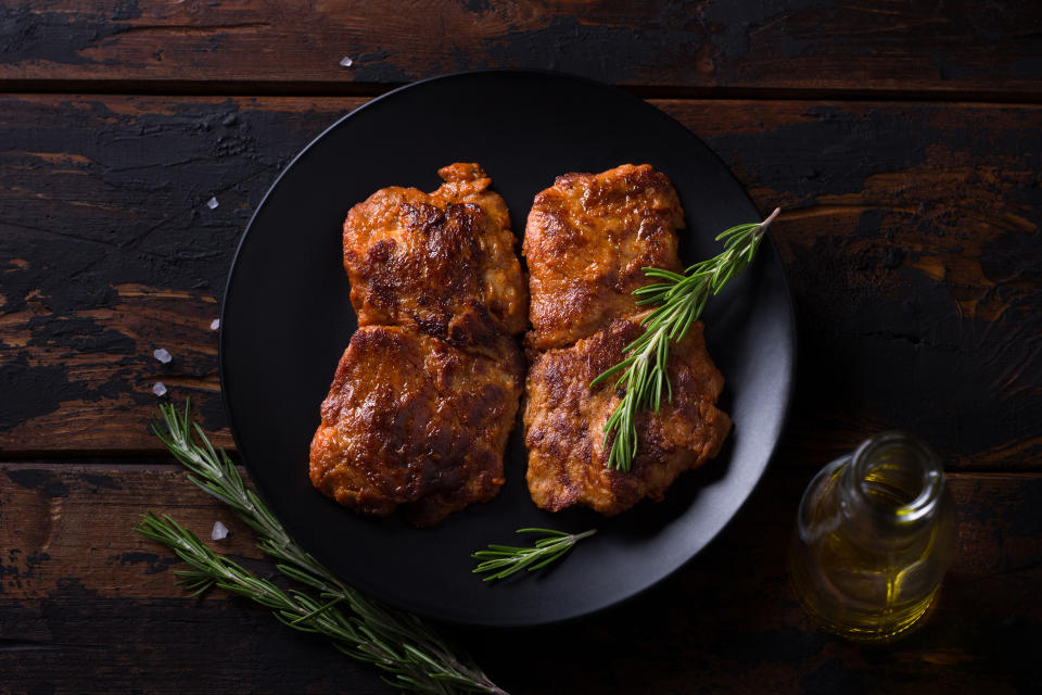 Fried vegan soy steak with rosemary, salt and pepper on black plate on wooden background, top view