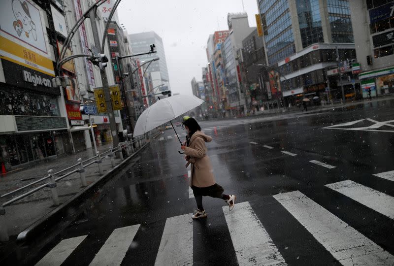 A woman wearing a protective face mask, following an outbreak of the coronavirus disease, walks past on a nearly empty street in a snow fall in Tokyo