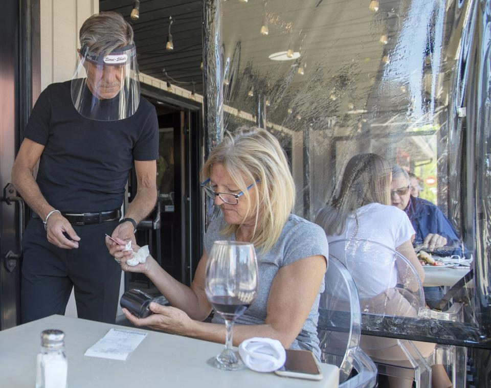 A waiter wearing protective equipment collects the bill