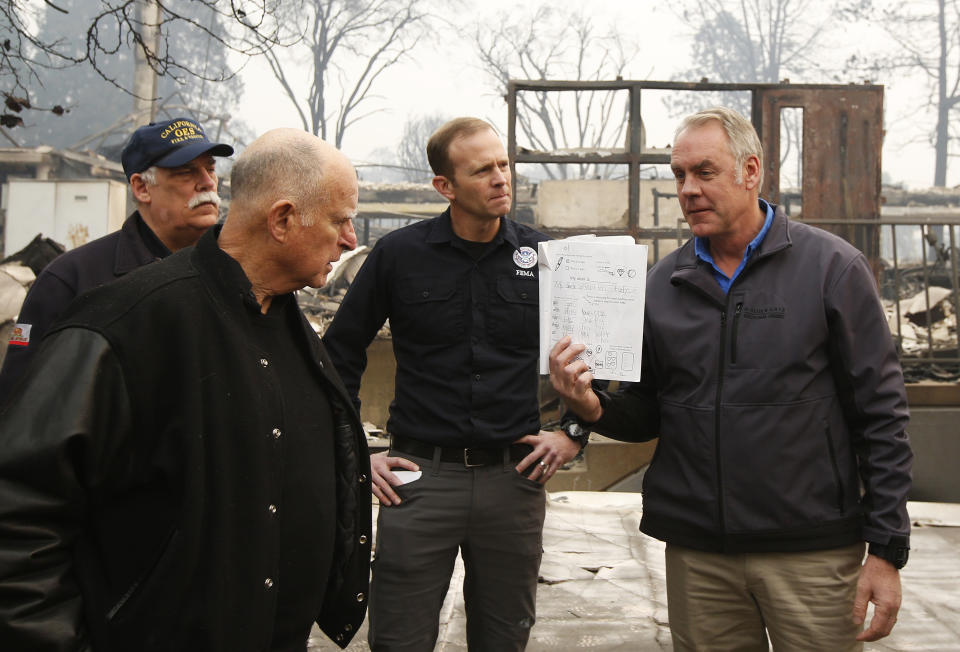 FILE — California Gov. Jerry Brown, second from left, looks at a students work book displayed by Interior Secretary Ryan Zinke, that was found during a tour of the fire ravaged Paradise Elementary School on Nov. 14, 2018, in Paradise, Calif. Brown has called California's mega fires "the new abnormal" as climate change turns the state warmer and drier. With the help of Ken Pimlott, the former chief of the California Department of Forestry and Fire Protection, Brown convened a group at his rural Colusa County ranch in September 2021, to discuss what could be done to save California's forests. (AP Photo/Rich Pedroncelli, File)