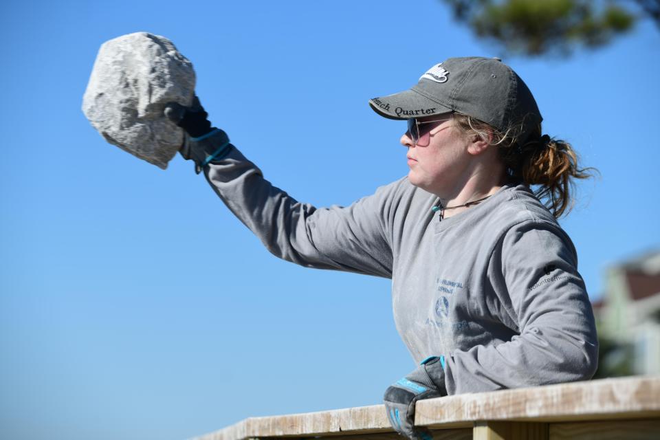 AmeriCorps member Katriona Hajduk lobs a limestone rock over the boardwalk rail at Liza Jackson Park as she and others build breakwaters at the park as part of a Choctawhatchee Basin Alliance project.