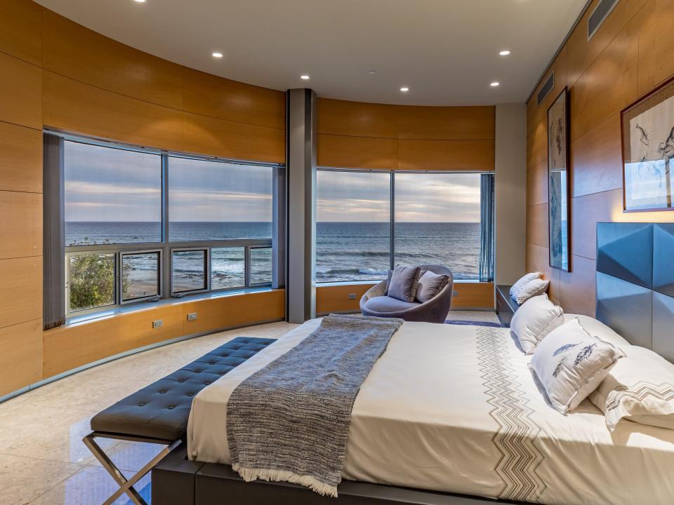 A bedroom with a large wrapped window that looks to the sea.