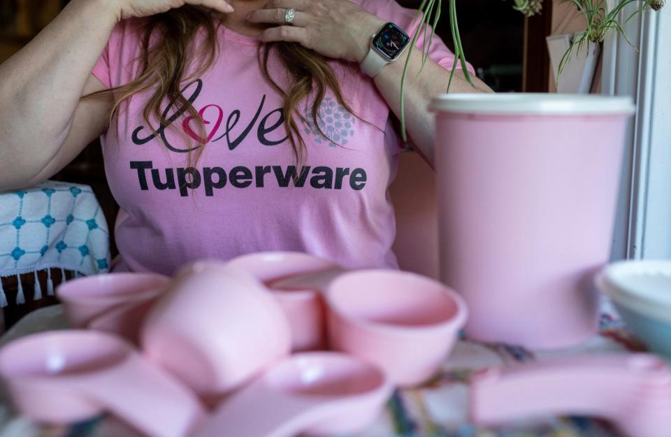 Janet Henriksen Lloyd, a Tupperware consultant and stay-at-home mother of four, fixes her hair as she sits on a table filled with bright pink measuring cubs and a container inside her home in Davison on Friday, May 26, 2023. 