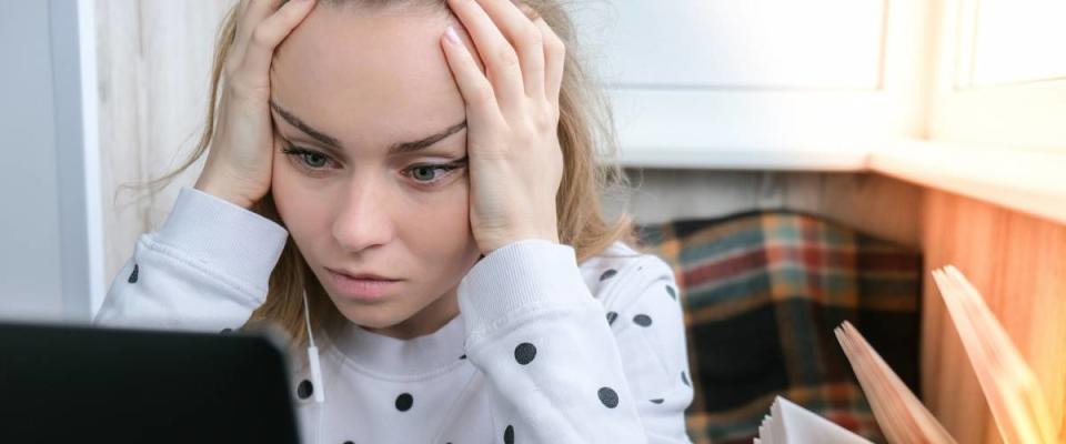 Young woman sitting on balcony next to laptop stressed over her student loan debt.