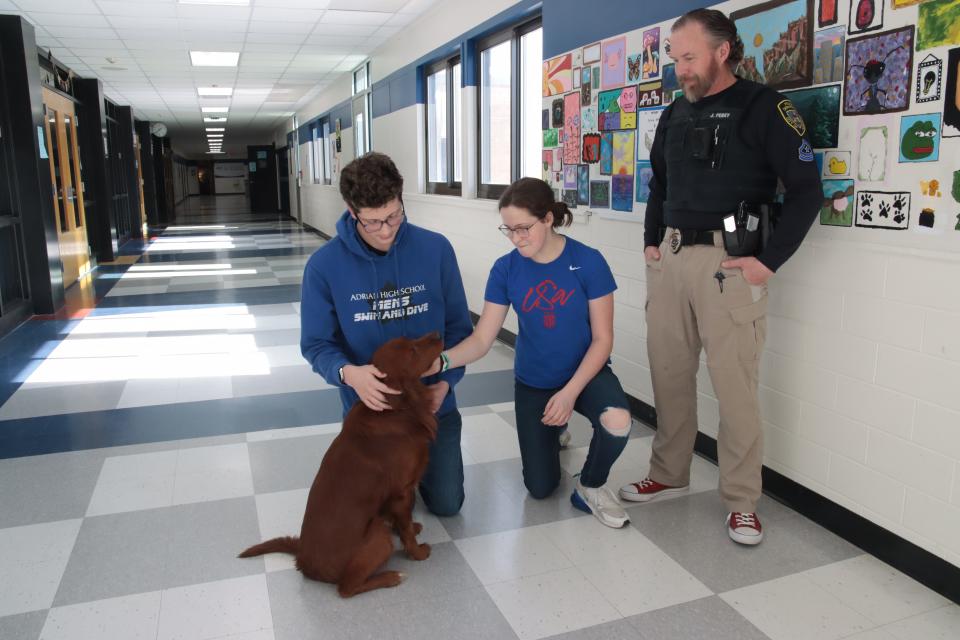 Adrian School Resource Officer Joshua Perry, right, watches as Adrian High School sophomores Noah and Claire Judson pet Charlie, the Adrian school district's police and therapy dog Feb. 7. The Tecumseh Board of Education voted Monday to buy its own police and therapy dog.