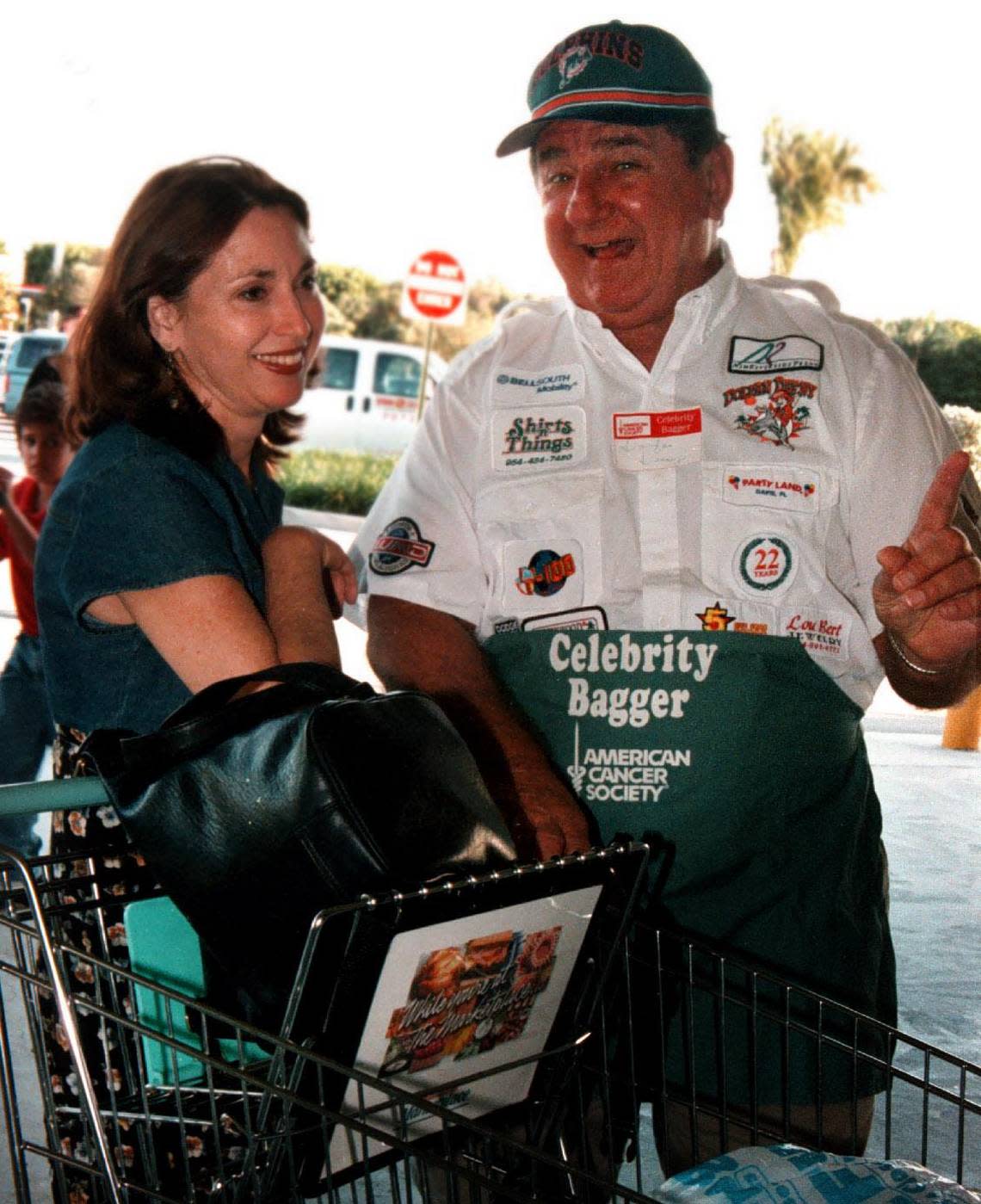 To Broward 01/03/99 Pembroke Pines resident Beverly Faubert gets talked into buying extra groceries Wednesday by South Florida sports celebrity Denny “Dolfan Denny” Sym, of Davie, at Winn Dixie on Pines Boulevard near 184th Street during celebrity bagging day held to benefit the American Cancer Society. Approximately 25 stores in Broward and dozens of local government officials, civic organization leaders, television and radio personalities and others notable neighbors participated in the event Five percent of purchases plus separate donations went toward the ACS fight against cancer.