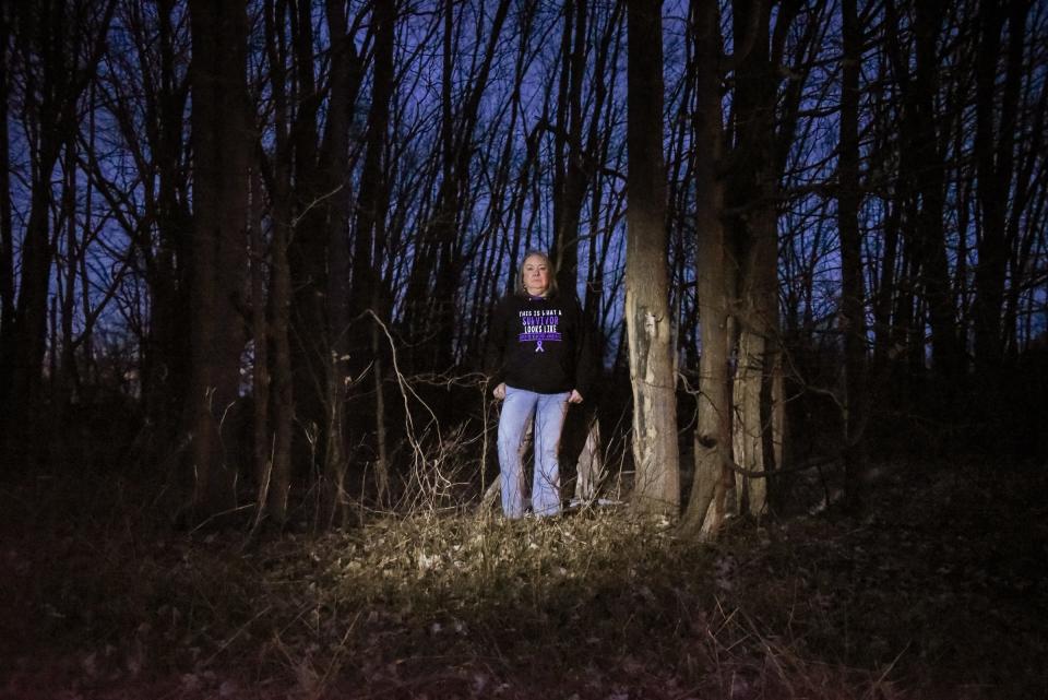 Stacy Balmes of Mason stands among a group of trees near the intersection of Kinneville and Tuttle roads, near Leslie on Monday, March 18, 2024. In 2019, her then-husband crashed his truck after he'd been drinking. She came to the scene and later lied to police and said she was driving the truck. She said it was one of several instances in which she felt forced to lie to protect herself and her children.