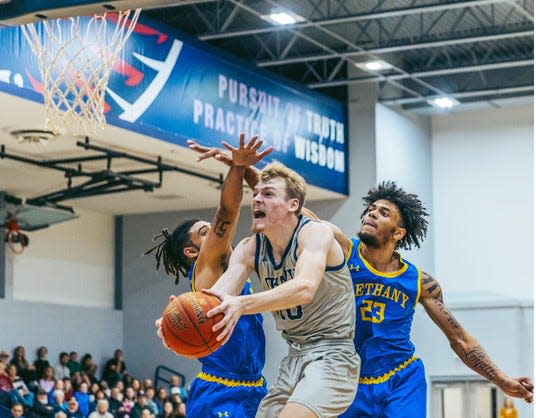 Oklahoma Wesleyan's Kaleb Stokes, center, powers through the air to the basket and draws the foul during Tuesday night's game against Bethany on Nov. 22, 2022.