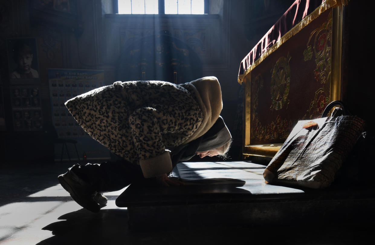 A woman kneeling at a church bends over to pray.