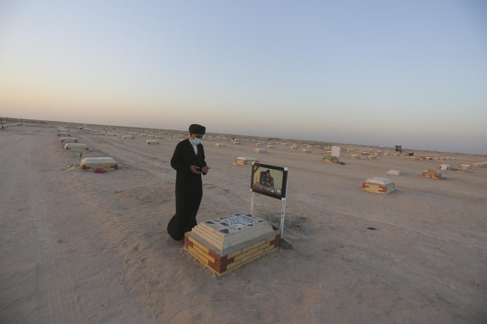 Shiite cleric prays by the grave of coronavirus victim at Wadi al-Salam cemetery near Najaf, Iraq, Sunday, July 19, 2020. A special burial ground near the Wadi al-Salam cemetery has been created specifically for COVID-19 victims since rejections of such burials have continued in Baghdad cemeteries and elsewhere in Iraq. (AP Photo/Anmar Khalil)