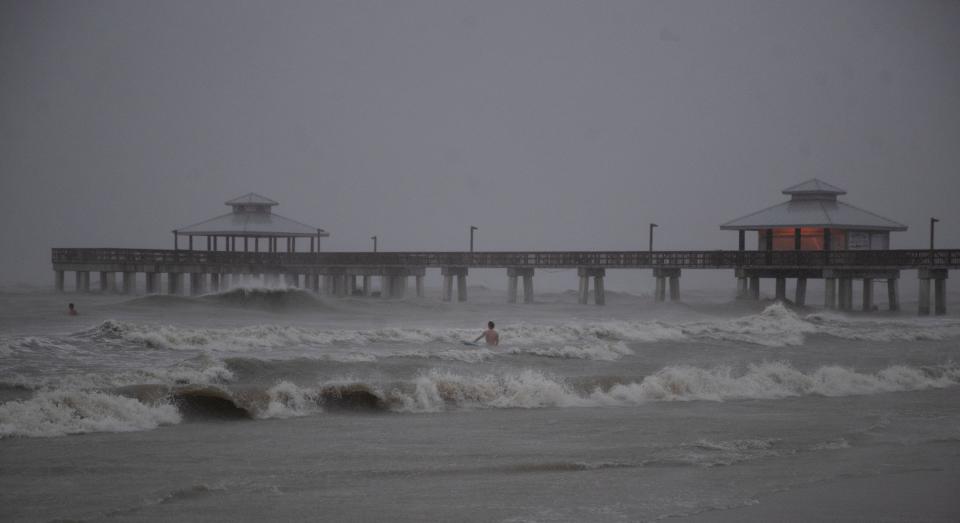 Surfers try to ride waves associated with Hurricane Ian on Sept. 28, 2022.  The pier would be destroyed hours after this photo was taken.