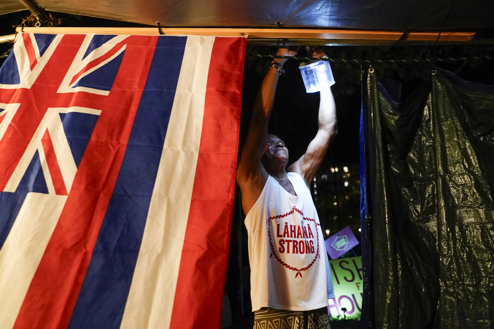 Naldo Valentine, who lost his home to the Lahaina wildfire, puts up a light as darkness falls at a housing protest on Kaanapali Beach Wednesday, Dec. 6, 2023, in Lahaina, Hawaii. A group of survivors is camping on the resort beach to protest and raise awareness for better long-term housing options for those displaced. Residents and survivors still dealing with the aftermath of the August wildfires in Lahaina have mixed feelings as tourists begin to return to the west side of Maui, staying in hotels still housing some displaced residents. (AP Photo/Lindsey Wasson)