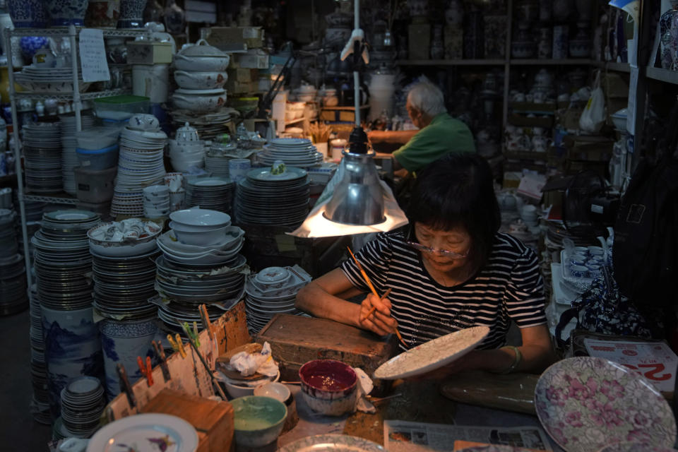 Staff members work at the Yuet Tung China Works, Hong Kong's last hand-painted porcelain factory, in Hong Kong, Wednesday, June 8, 2022. Step into Yuet Tung China Works, Hong Kong’s last remaining hand-painted porcelain factory, and you find yourself surrounded by stacks of dinnerware, each piece painstakingly decorated by hand with vibrant motifs of flowers, fruits and animals. (AP Photo/Kin Cheung)