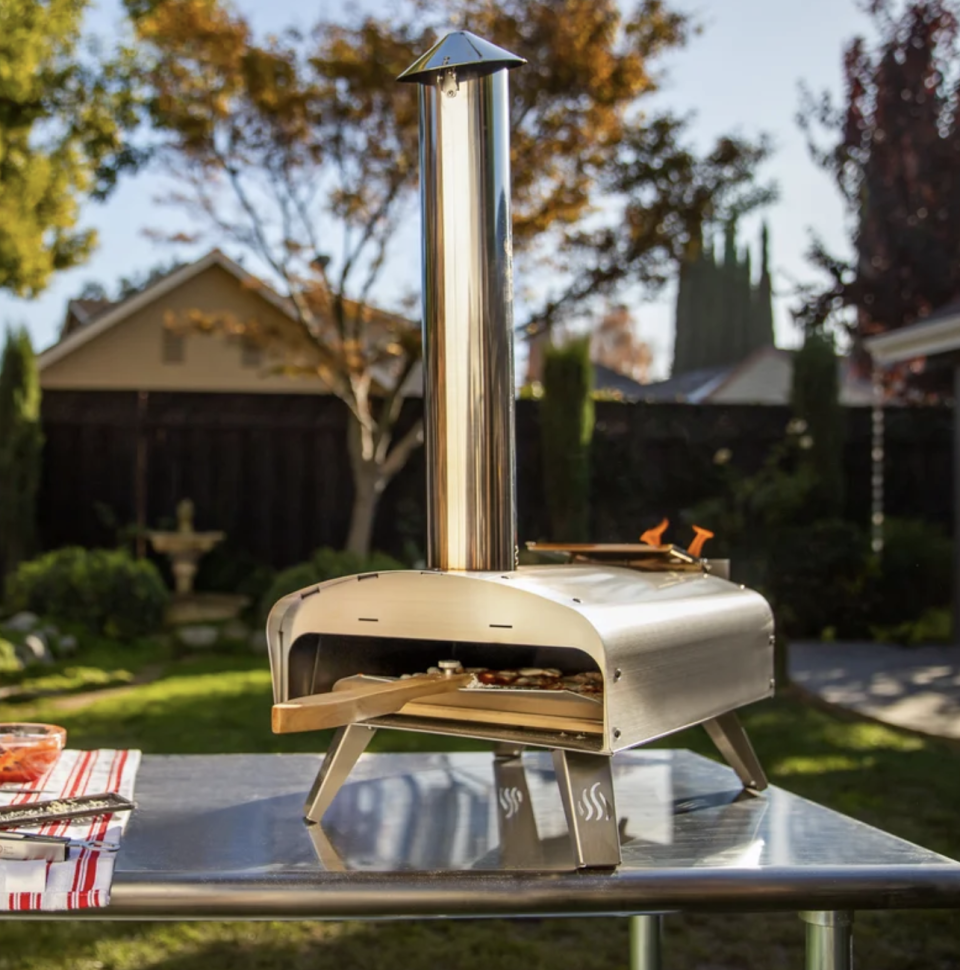 Mimiuo Portable Wood Pellet Pizza Oven in stainless steel on metal table in backyard (Photo via Wayfair)