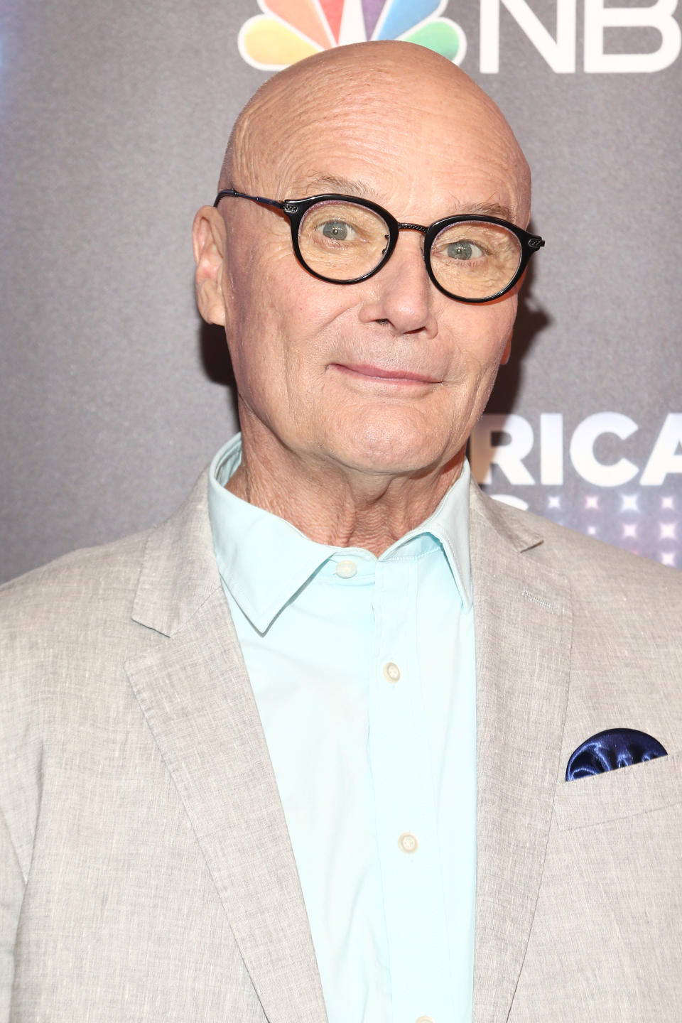 Creed Bratton wearing a light suit jacket, blue shirt, and glasses at an NBC event