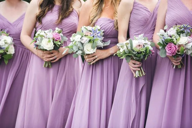 <p>Getty</p> Bridesmaids in pink and vioilet dresses holding floral arrangements