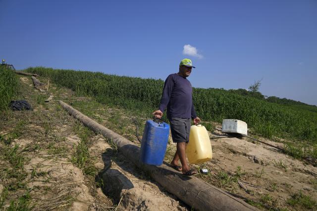 Jose Alves de Morais carries jugs to a boat in Lago Serrado community, near Carauari, Brazil, Thursday, Sept. 1, 2022. A Brazilian non-profit created a model for land ownership that welcomes both local people and scientists to collaborate in preserving the Amazon. "This is something that doesn't exist here in the Amazon, it doesn't exist anywhere in Brazil. If it works, which it will, it will attract a lot of people's attention," Morais, a resident, told the Associated Press. (AP Photo/Jorge Saenz)