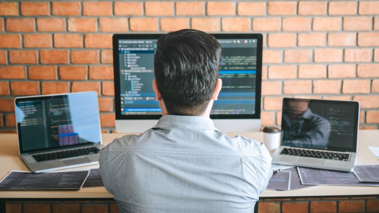  A person coding on a desktop computer and two laptops. 