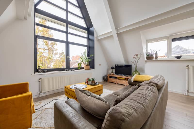 Brown suade couch, A frame ceiling with large picture window, orange modern armchair with matching ottoman/coffee table, low wood tv console