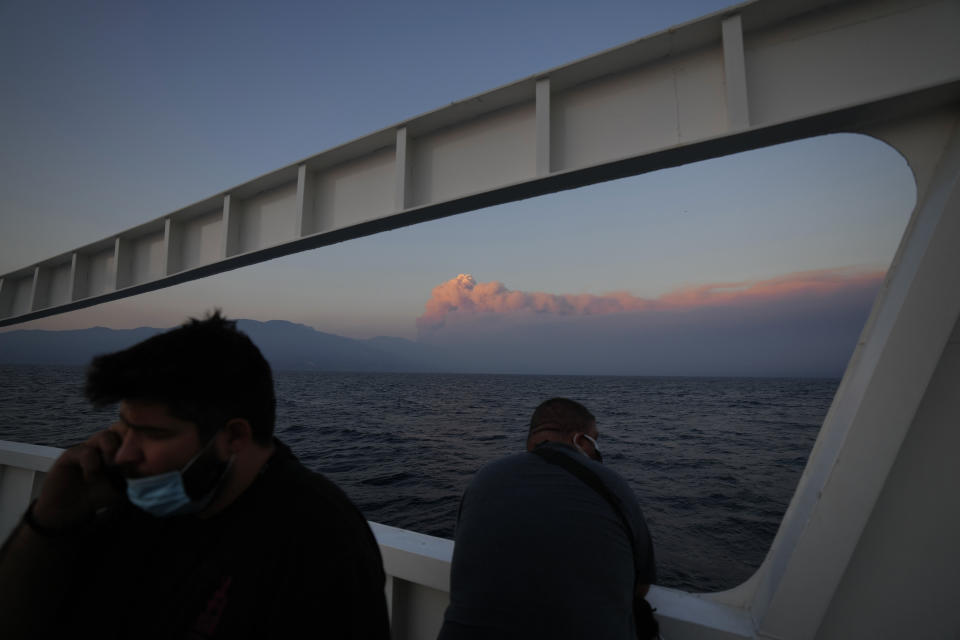 A man speaks from his phone onboard a ferry as a huge cloud, is seen in the background, of smoke fills the horizons at sun set over the island of Evia, where catastrophic wildfires continue to burn, about 160 kilometers (100 miles) north of Athens, Saturday, Aug. 7, 2021. Wildfires rampaged through massive swathes of Greece's last remaining forests for yet another day Saturday, encroaching on inhabited areas and burning scores of homes, businesses and farmland. (AP Photo/Petros Karadjias)
