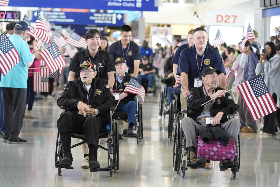 World War II veterans Art Leach, front right, and Henry Armstrong, front left, are pushed along by Colin Renick, right, and Ye Jin Bae as they make their way to board a plane with others at Dallas Fort Worth International Airport in Dallas Friday, May 31, 2024. A group of World War II veterans are being flown from Texas to France where they will take part in ceremonies marking the 80th anniversary of D-Day. (AP Photo/LM Otero)