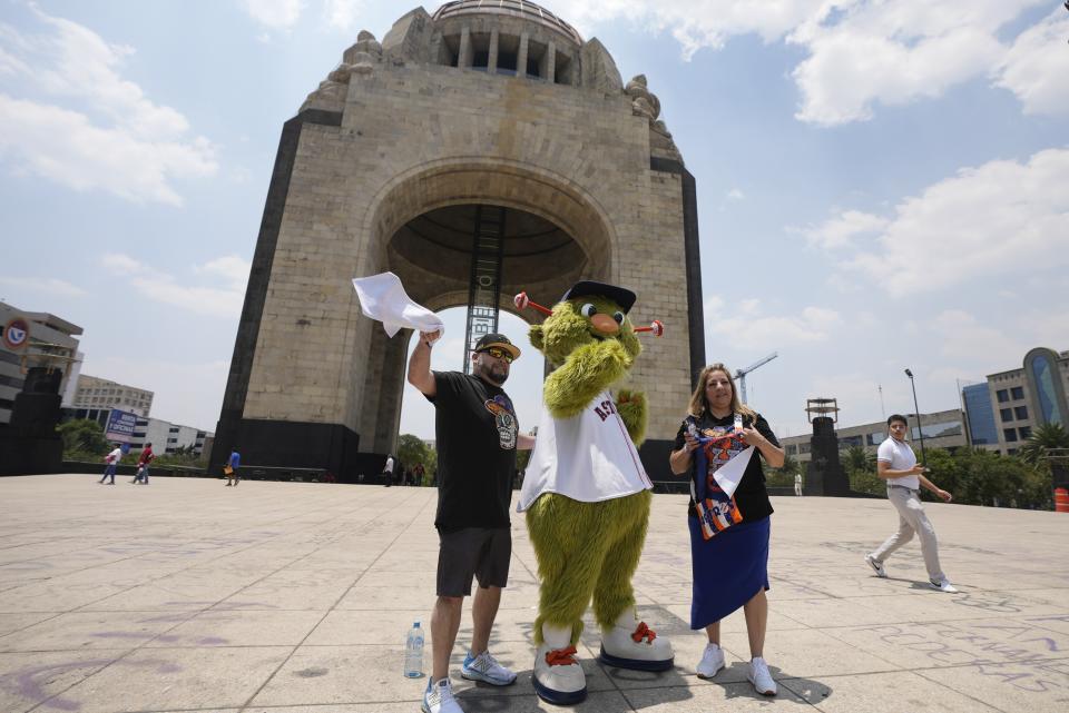 Houston Astros team mascot Orbit and fans, pose for a photo backdropped by the Monument to the Revolution in Mexico City, Thursday, April 25, 2024. The Houston Astros will face Colorado Rockies in two regular season game beginning Saturday, at Mexico City's Alfredo Harp Helú stadium. (AP Photo/Fernando Llano)