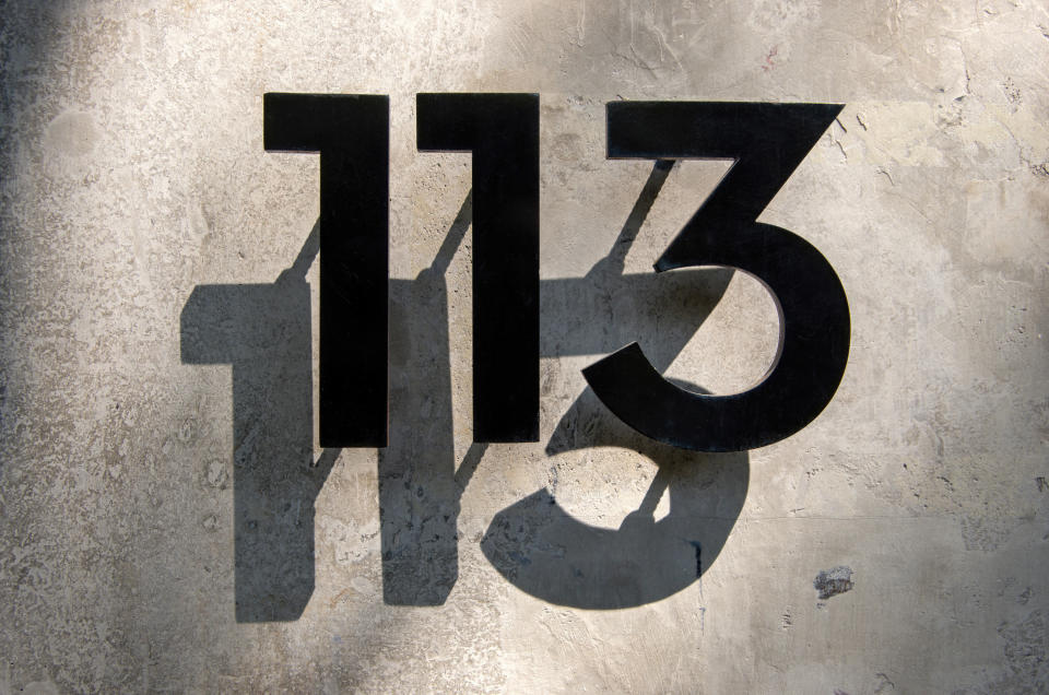 Metal house number "113" in front of a concrete wall