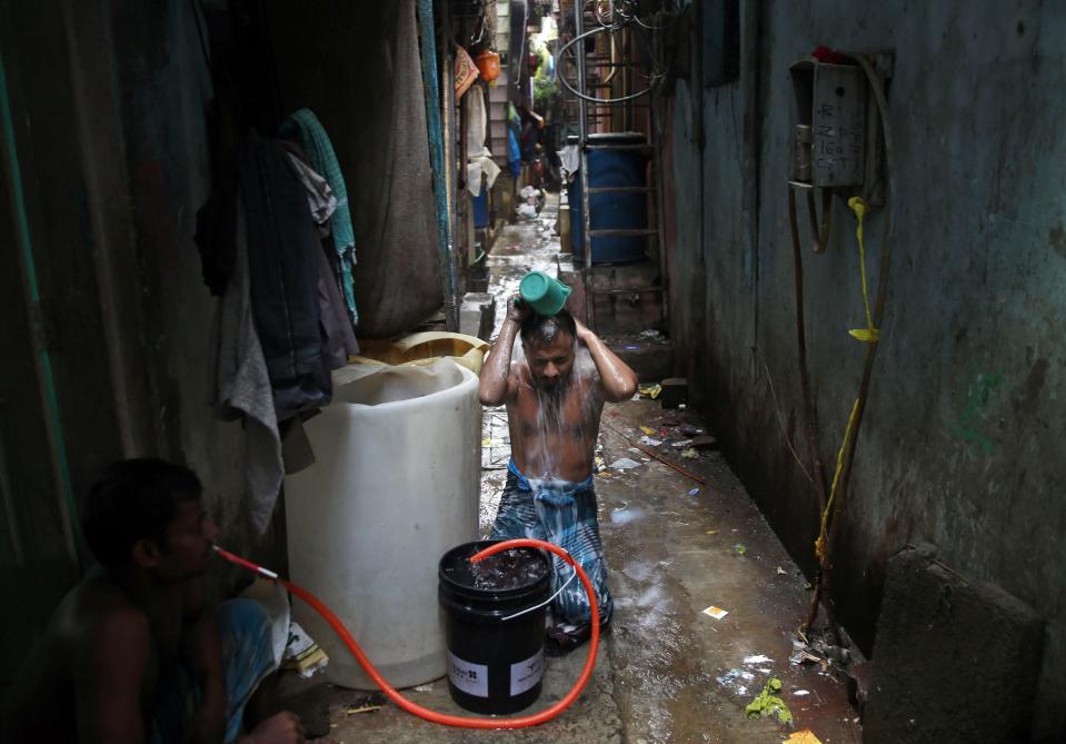 FILE - In this Thursday, July 10, 2014, file photo, a man bathes outside his house in Dharavi, one of Asia's largest slums, in Mumbai, India. Set between busy train tracks and the heavily polluted Mithi River, which separates the slum from Mumbai’s modern skyscrapers, the neighborhood is a maze of tiny alleys, each one full of scores of people who live in tin shacks. Families or groups of migrant workers often pile into a single room. Hardly anyone has a private bathroom. (AP Photo/Rafiq Maqbool, File)