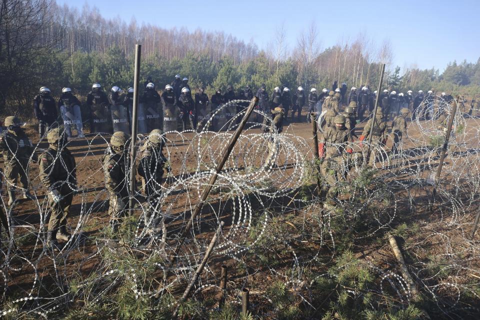 Polish police and border guards stand near the barbed wire as migrants from the Middle East and elsewhere gather at the Belarus-Poland border near Grodno Grodno, Belarus, Tuesday, Nov. 9, 2021. Hundreds if not thousands of migrants sought to storm the border from Belarus into Poland on Monday, cutting razor wire fences and using branches to try and climb over them. The siege escalated a crisis along the European Union's eastern border that has been simmering for months. (Leonid Shcheglov/BelTA via AP)