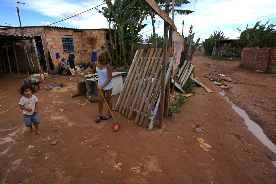 A young woman sweeps the dirt path outside her home in the Sol Nascente favela of Brasilia, Brazil, Wednesday, March 22, 2023. The growth of Sol Nascente, which means Rising Sun, reflects people moving here in search of cheap or unoccupied land to build homes, whereas elsewhere in the Federal District poor people often pay relatively high rents. (AP Photo/Eraldo Peres)