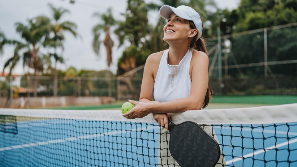 Woman laughing and smiling holding pickleball bat on court