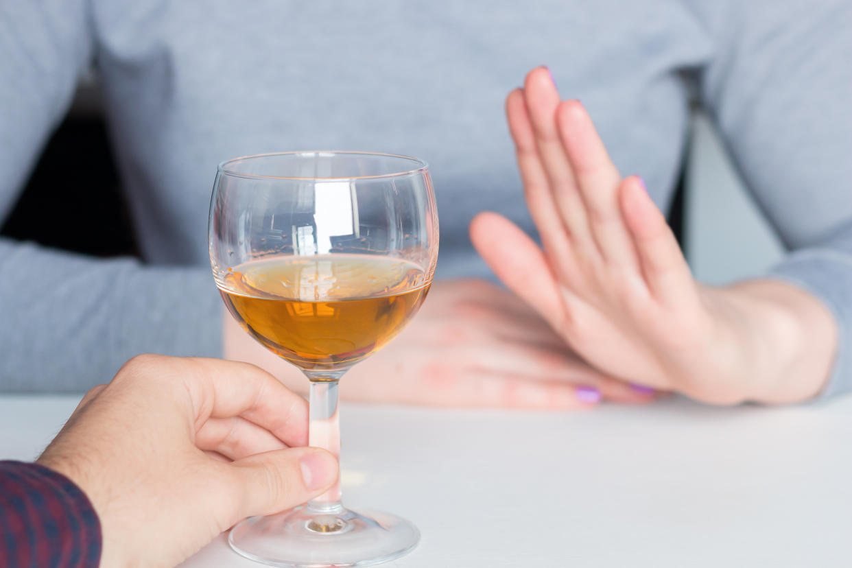 A hand forms the sign for stop when a wineglass is offered by another hand